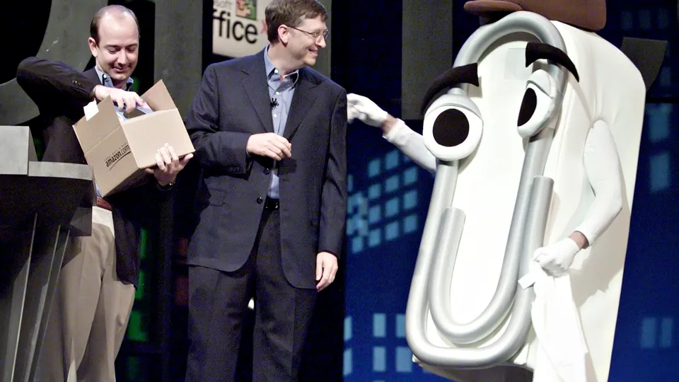 Bill Gates presents a T-shirt as a retirement gift to a person dressed as Clippy while Amazon CEO Jeff Bezos looks on, at the Office XP launch in New York on May 31, 2001.