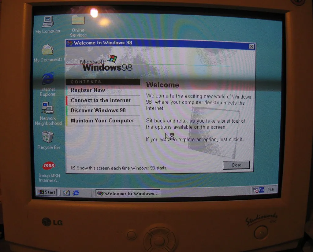 A beige LG CRT monitor showing the Windows 98 desktop with the Welcome to Windows 98 window open, listing Register Now, Connect to the Internet, Discover Windows 98, and Maintain Your Computer.